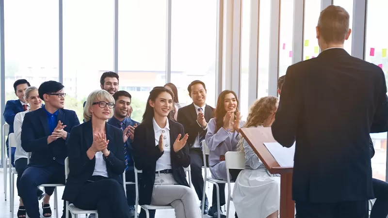 Business professionals applauding at a conference, showing appreciation and support for the speaker.