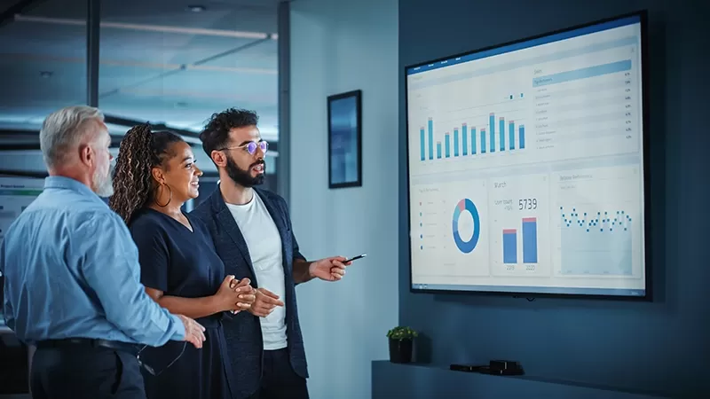 Three individuals standing in front of a massive screen, engaged in an activity or presentation.