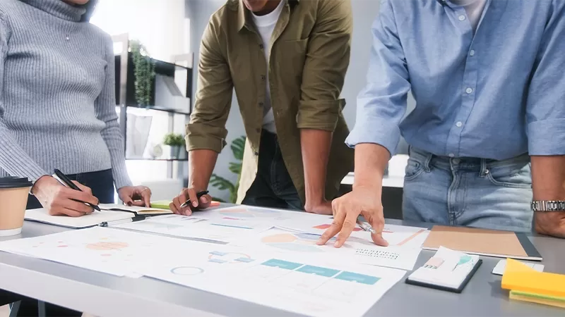 Team standing around a table looking at plans